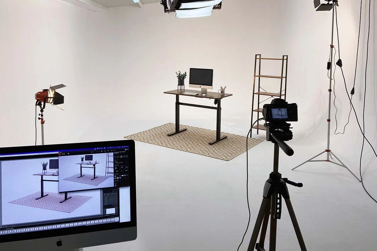 A desk on a white studio set with lighting and a production monitor